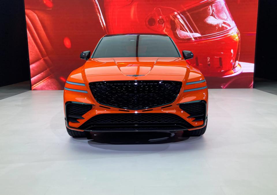 An orange Genesis GV80 Coupe concept SUV shown from the front, with a red backdrop.