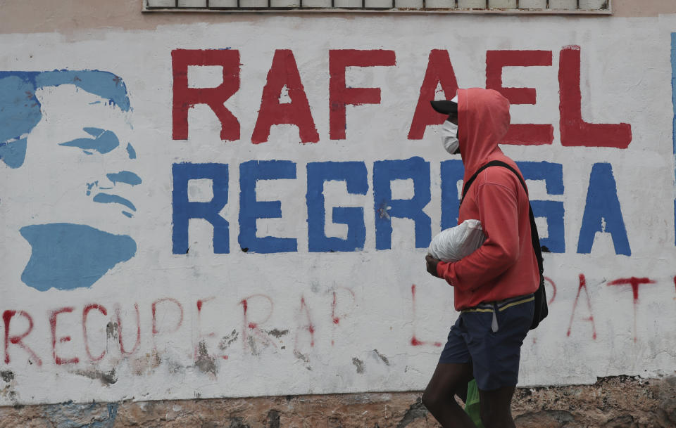 Un hombre con una máscara de protección en medio de la pandemia del nuevo coronavirus camina junto a un letrero a favor del regreso del expresidente de Ecuador, Rafael Correa, en Quito, Ecuador, el martes 7 de abril de 2020. El Tribunal de la Corte Nacional de Justicia de Ecuador declaró el martes culpable de corrupción a Correa y lo sentenció a ocho años de prisión. (AP Photo/Dolores Ochoa)