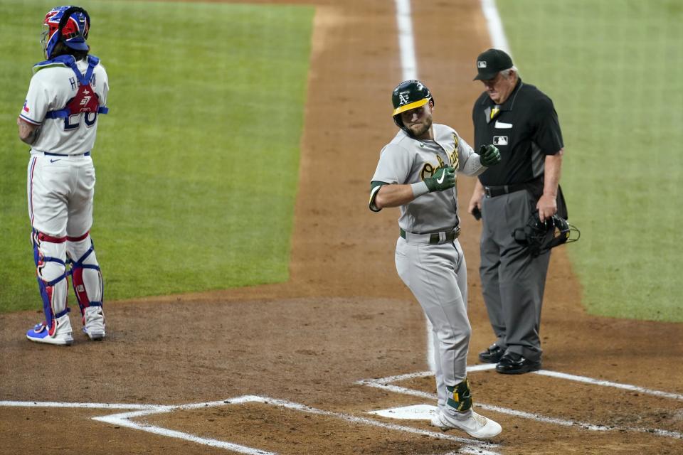 Oakland Athletics' Seth Brown, center, crosses the plate after hitting a solo home run as umpire Joe West, right, and Texas Rangers catcher Jonah Heim stand by in the second inning of a baseball game in Arlington, Texas, Saturday, July 10, 2021. (AP Photo/Tony Gutierrez)