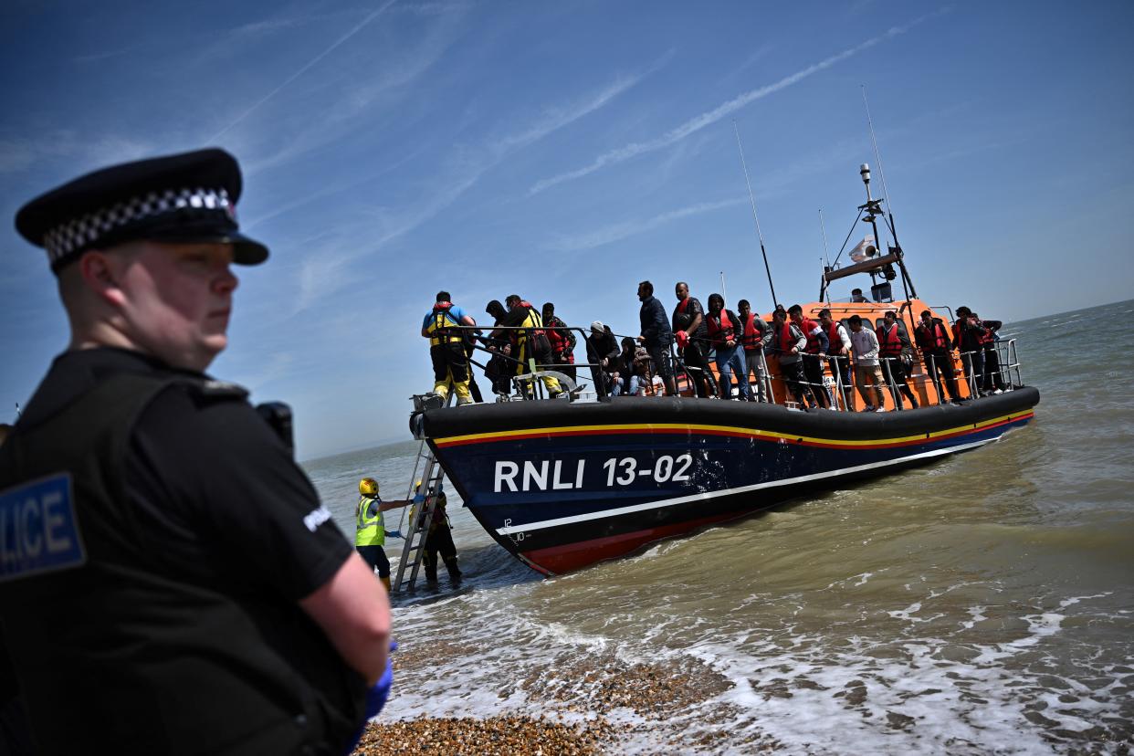 TOPSHOT - A British police officer stands guard on the beach of Dungeness, on the southeast coast of England, on June 15, 2022, as Royal National Lifeboat Institution's (RNLI) members of staff help migrants to disembark from one of their lifeboat after they were picked up at sea while attempting to cross the English Channel. - Furious Conservatives called on Britain's government on June 15, 2022 to abandon a European human rights pact after a judge dramatically blocked its plan to fly asylum-seekers to Rwanda. Under the UK's agreement with Rwanda, all migrants arriving illegally in Britain are liable to be sent to the East African nation thousands of miles away for processing and settlement. The government, after arguing that Brexit would lead to tighter borders, says the plan is needed to deter record numbers of migrants from making the perilous Channel crossing from northern France. (Photo by Ben Stansall / AFP) (Photo by BEN STANSALL/AFP via Getty Images)