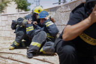 Israeli firefighters take cover as a siren sounds a warning of incoming rockets fired from the Gaza strip, in the southern Israeli town of Ashkelon, Tuesday, May 11, 2021. (AP Photo/Ariel Schalit)