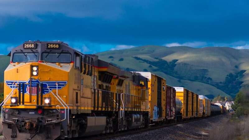 Train runs on tracks with blue sky and a mountain in the background