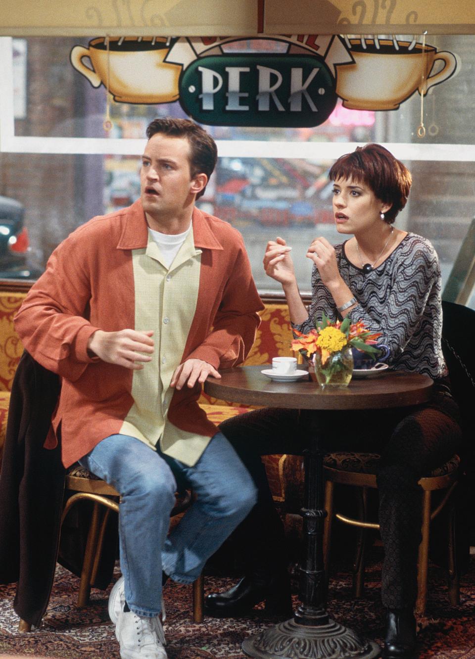 Paget Brewster and Matthew sitting at a table in a coffee shop in a scene from "Friends"