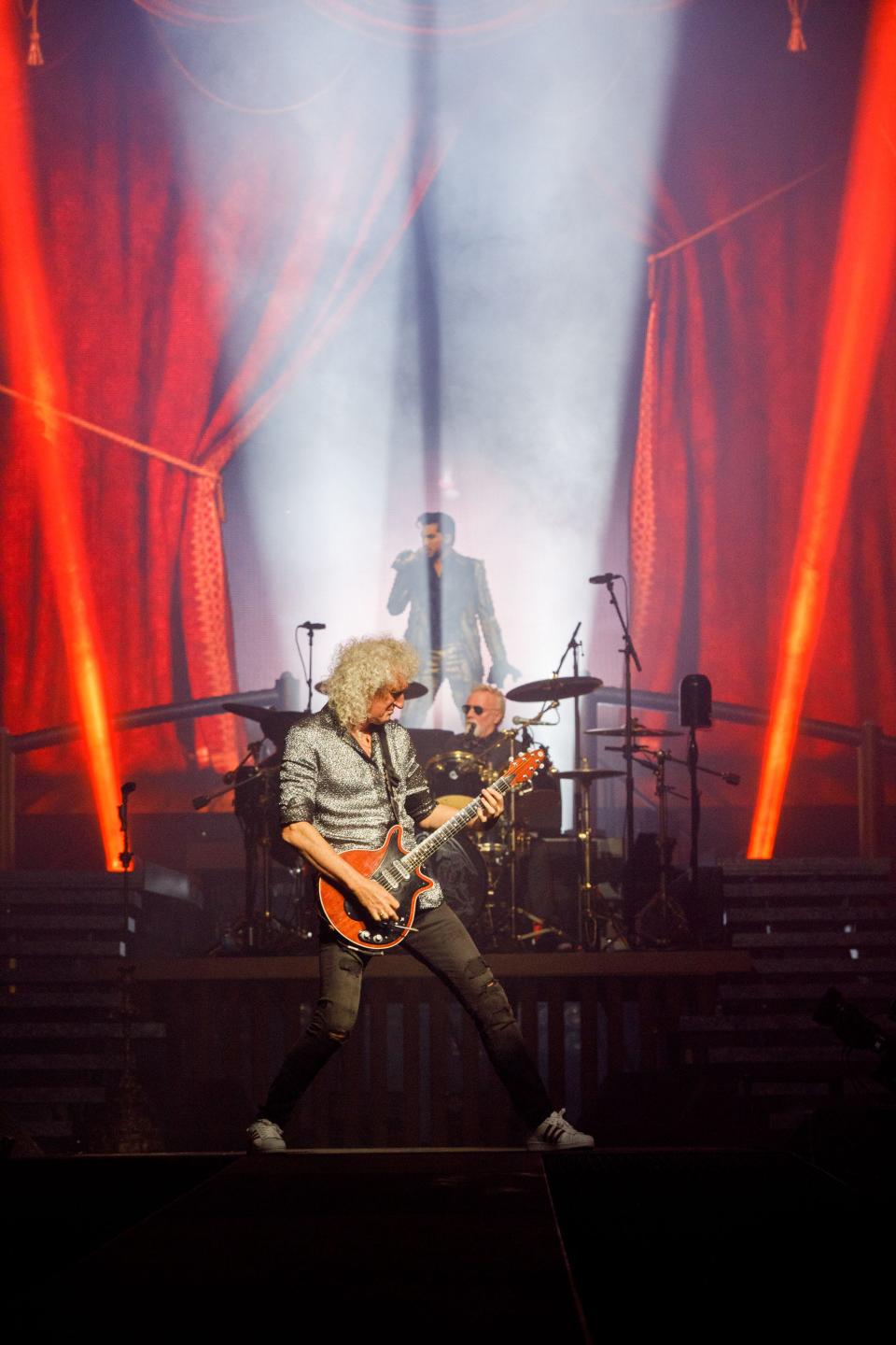 Brian May - recently knighted by King Charles - strikes his trademark pose while original Queen drummer Roger Taylor and singer Adam Lambert perform behind him.