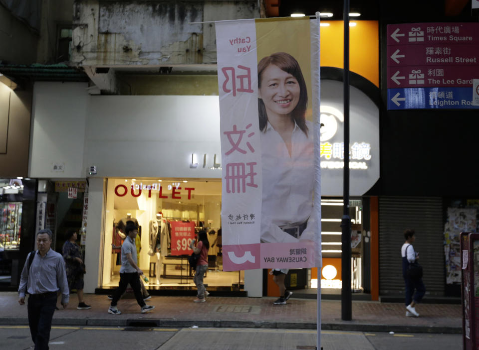 In this photo taken Thursday, Nov. 7, 2019, people walk past the campaign banner for district council candidate Cathy Yau at Causeway Bay in Hong Kong. Yau. a former police officer, grew exasperated as police used more force to quell the unrest. She quit the force in July after 11 years and is running in Sunday's district polls that are widely expected to deliver a decisive victory for the six-month-old movement seeking democratic reforms in the semi-autonomous Chinese territory. (AP Photo/Dita Alangkara)