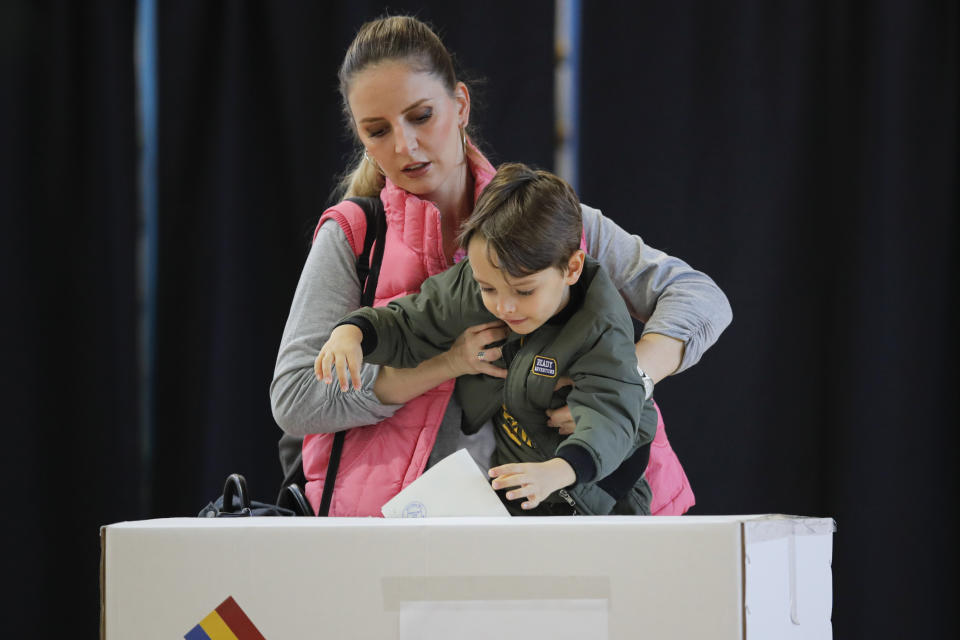 A woman holds a child to cast her vote in Bucharest, Romania, Sunday, Nov. 10, 2019. Voting got underway in Romania's presidential election after a lackluster campaign overshadowed by a political crisis which saw a minority government installed just a few days ago. (AP Photo/Vadim Ghirda)