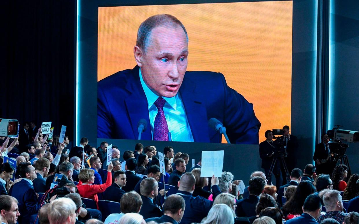 A video screen displays Russian President Vladimir Putin speaking during his annual press conference in Moscow while journalists hold placards - AFP
