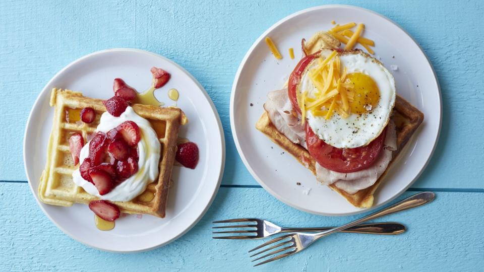 breakfast in bed plate of homemade waffles with strawberry topping and plate with eggs, tomato, deli meat, cheese