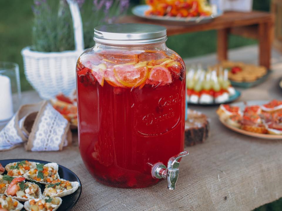 a big jar of red punch on a table full of plates of food