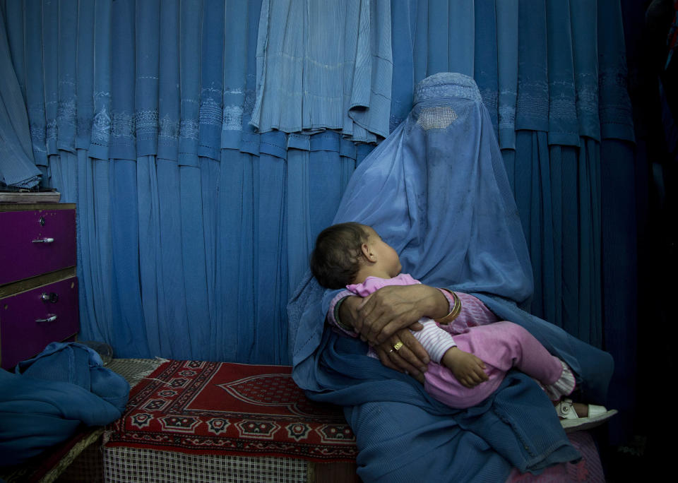 In this Thursday, April 11, 2013 photo, an Afghan woman waits with her child in front a changing room to try on a new burqa at a shop in the old town of Kabul, Afghanistan. Despite advances in women’s rights, Afghanistan remains a deeply conservative country and most women continue to wear the Burqa. But tradesmen say times are changing in Kabul at least, with demand for burqas declining as young women going to school and taking office jobs refuse to wear the cumbersome garments. (AP Photo/Anja Niedringhaus)