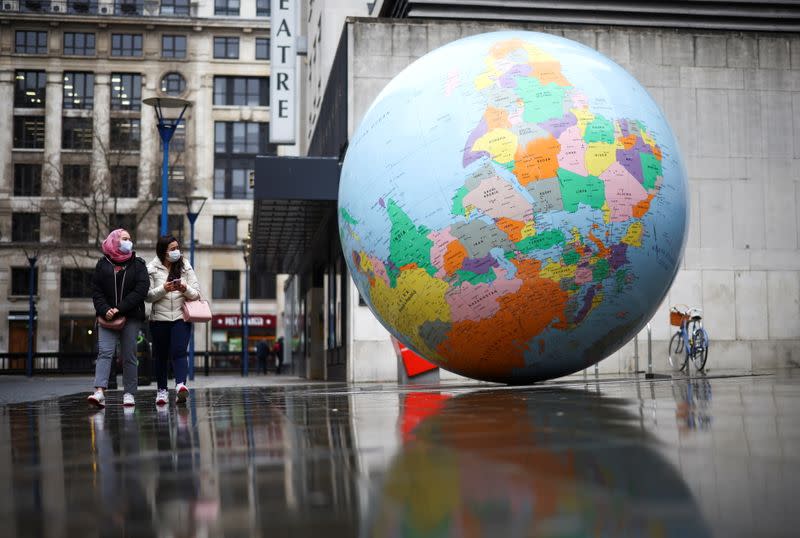 People wearing protective face masks walk past 'The World Turned Upside Down' sculpture by Mark Wallinger, in London