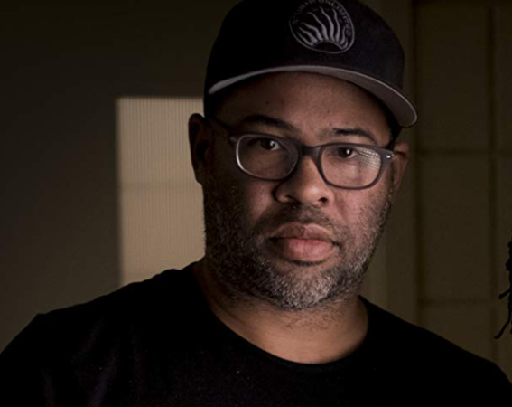 All of Jordan Peele's movies and other horror projects ranked. Pictured: A close-up shot of Jordan Peele wearing glasses and a hat. | 