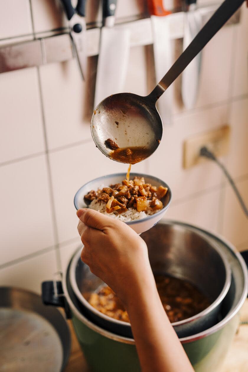 Scooping pork belly out of a metal pot onto a bowl of rice