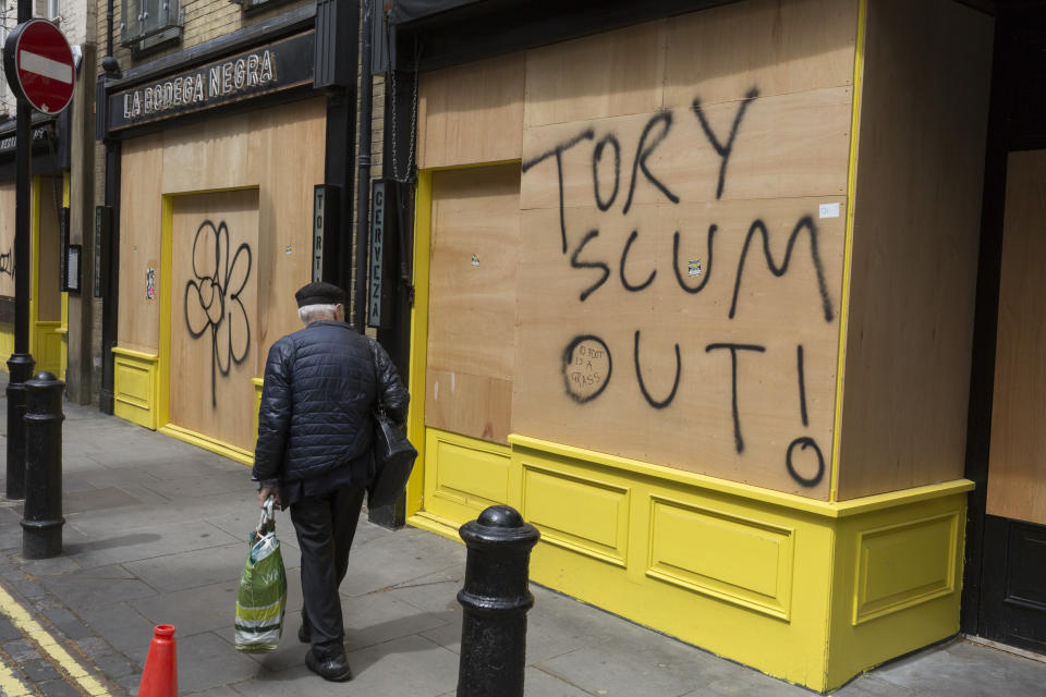 During the UK's Coronavirus pandemic lockdown and in the 24hrs when a further 255 deaths occurred, bringing the official covid deaths to 37,048, 
and seen the day after the very unusual press conference by UK Prime Minister's special advisor Dominic Cummings about his breaking of lockdown rules, an elderly man walks past the message "Tory Scum Out!" which has been written on plyboard on a closed business in Soho, on 26th May 2020, in London, England. (Photo by Richard Baker / In Pictures via Getty Images)