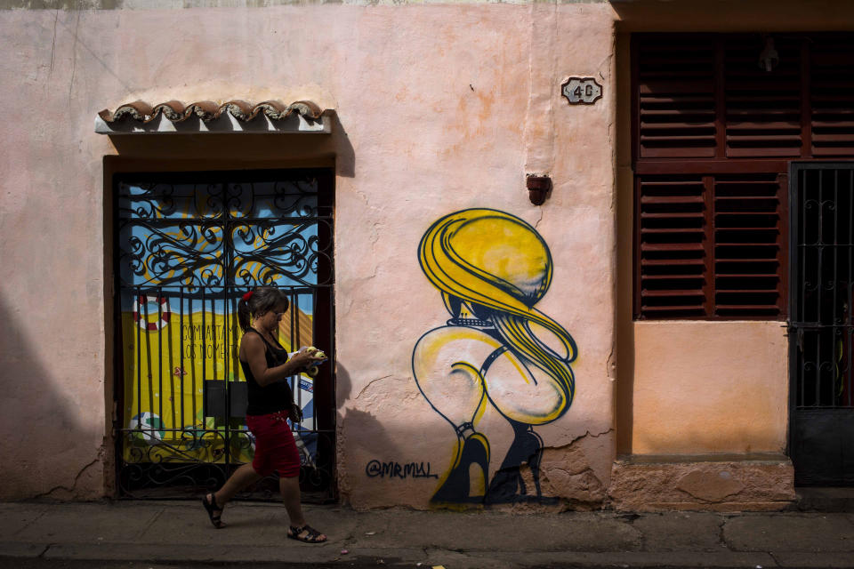 A woman passes by a closed art store decorated by a mural in Havana, Cuba, Wednesday, Dec. 5, 2018. After weeks of public debates and overlapping complaints from artists and intellectuals about a decree that increased control for artists and promoters, Cuban authorities are about to publicize complementary rules that limit the power of cultural inspectors and limit official action about creation. (AP Photo/Desmond Boylan)