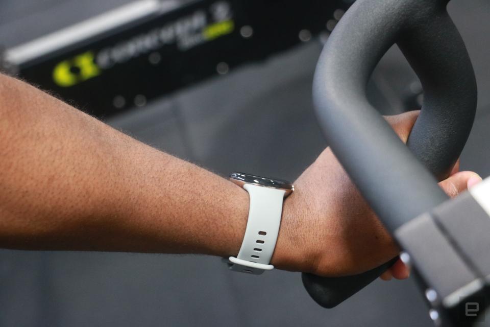 The Pixel Watch 2 on a person's wrist, while they grab onto the handlebars of a stationary bike. The back of the person's hand is pressing back onto the watch's dial.