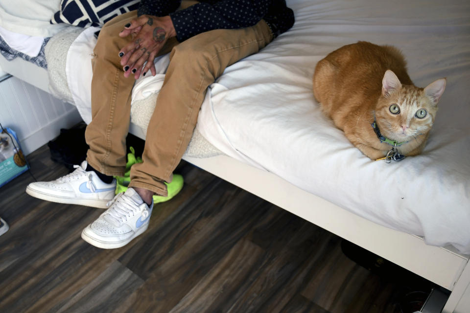 Eric Martinez sits with his cat in his room at a micro community in Denver on Wednesday, June 5, 2024. Martinez along with the others were directed into the micro communities of small cabin-like structures with a twin bed, desk and closet, after his Denver tent encampment was swept. The city built three such communities with nearly 160 units total in about six months, at roughly $25,000 per unit. (AP Photo/Thomas Peipert)