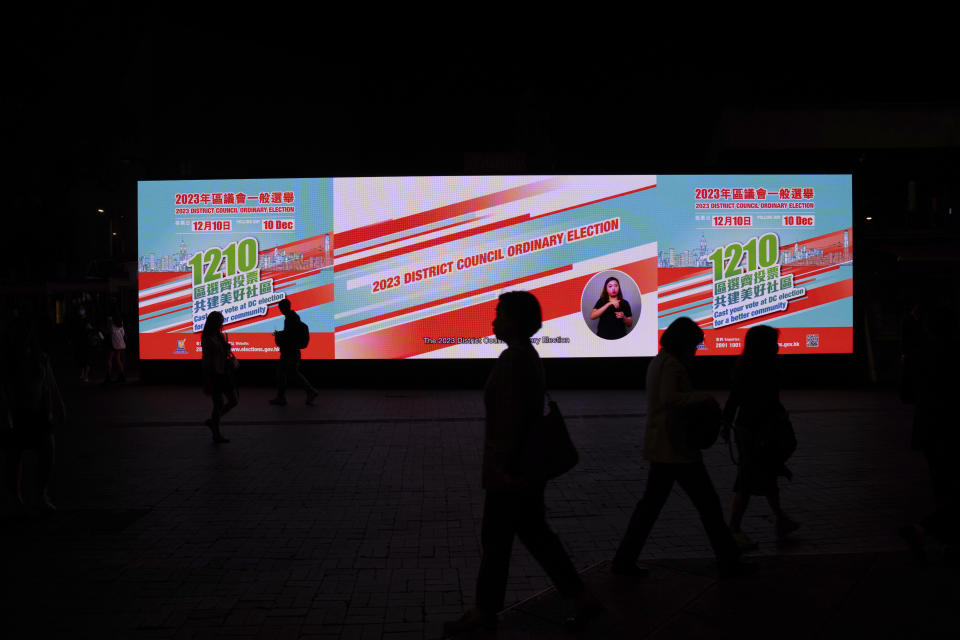 Pedestrians walk past an electronic billboard promoting the upcoming district council elections in Hong Kong, Tuesday, Nov. 28, 2023. (AP Photo/Louise Delmotte)