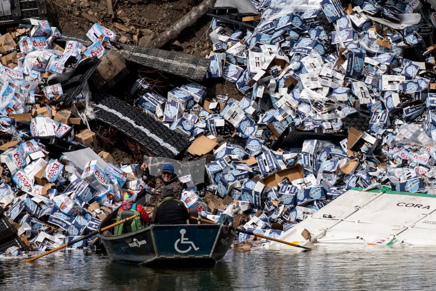 A group of fishermen claim a bottle of beer from a derailed railcar on the banks of the Clark Fork River near Quinn’s Hot Springs, west of St. Regis, Mont., Sunday, April 2, 2023. Montana Rail Link is investigating the derailment in which there were no injuries reported. (Ben Allan Smith/The Missoulian via AP)