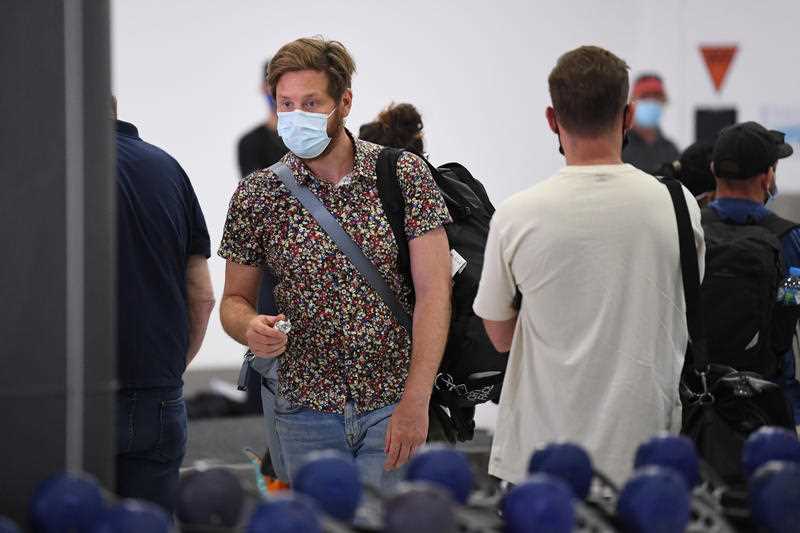 People wearing face masks are seen in the baggage collection area after arriving on Virgin Australia flight VA318 from Brisbane at Tullamarine Airport in Melbourne.