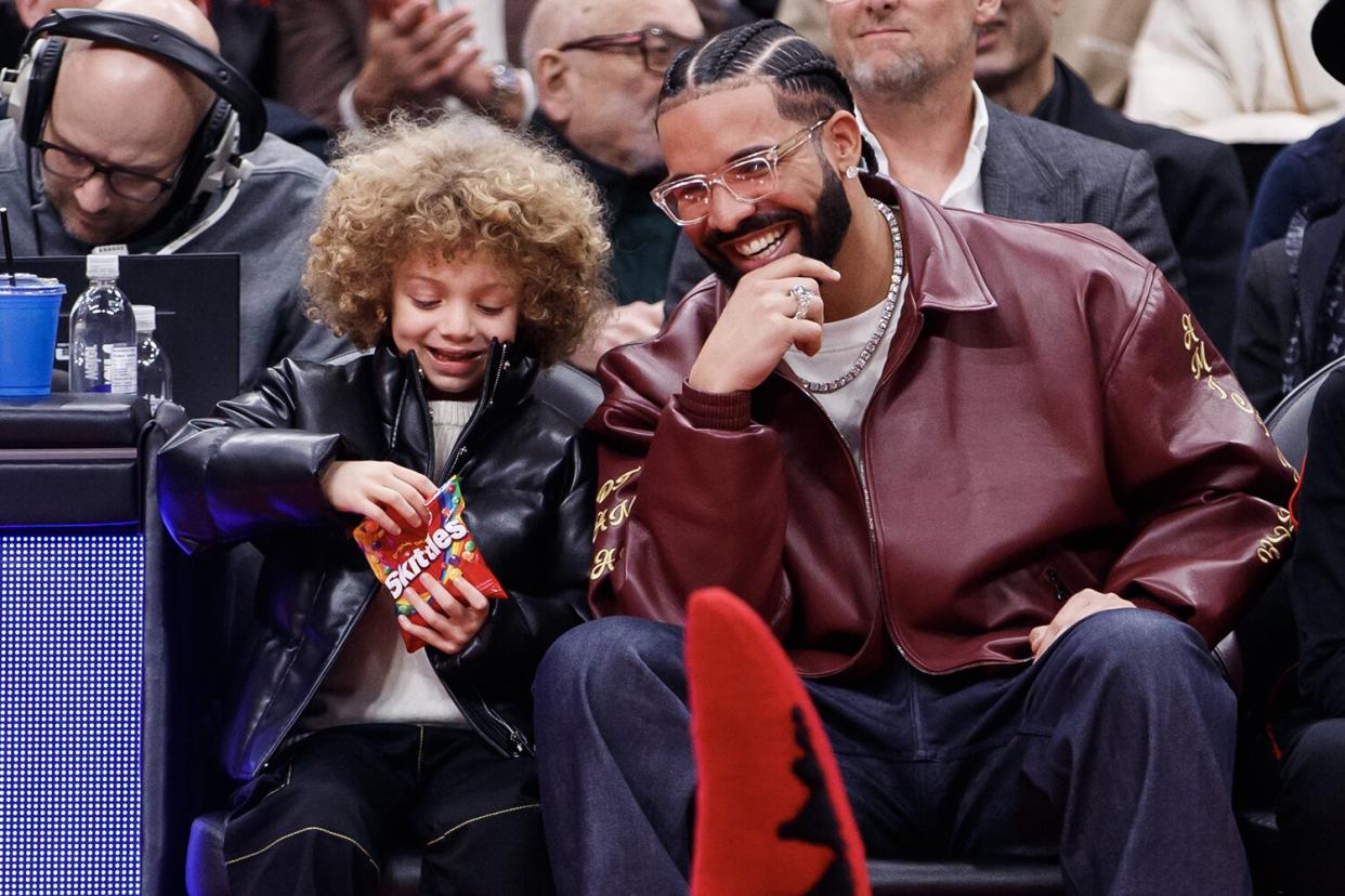 Drake and his son Adonis Graham watch as the Raptors mascot goofs around in front of them during a timeout in the first half of the NBA game between the Toronto Raptors and the Los Angeles Lakers