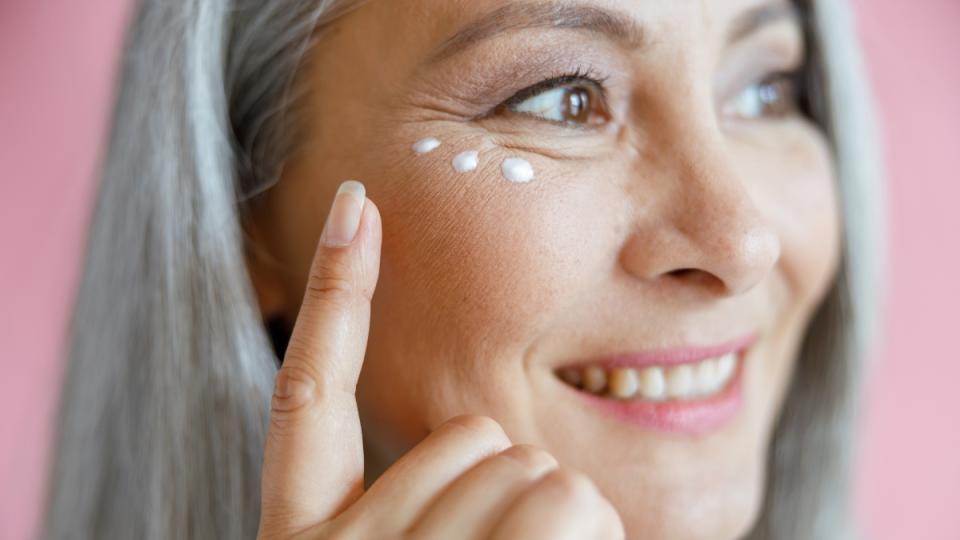 A woman with grey hair applying drops of sunscreen to her eye area