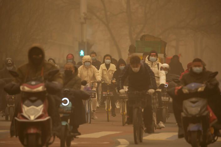 People ride bicycles across an intersection amid a sandstorm during the morning rush hour in Beijing, Monday, March 15, 2021. The sandstorm brought a tinted haze to Beijing's skies and sent air quality indices soaring on Monday. (AP Photo/Mark Schiefelbein)