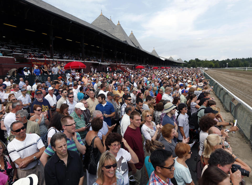 FILE- In this July 20, 2012 file photo, fans watch the fifth horse race on opening day at Saratoga Race Course in Saratoga Springs, N.Y. Saratoga Springs' racetrack is still going strong as it marks its 150th anniversary this summer, the centerpiece attraction in a town that's also known for mineral springs, Victorian charm and upscale hotels, shops and restaurants. (AP Photo/Mike Groll, File)