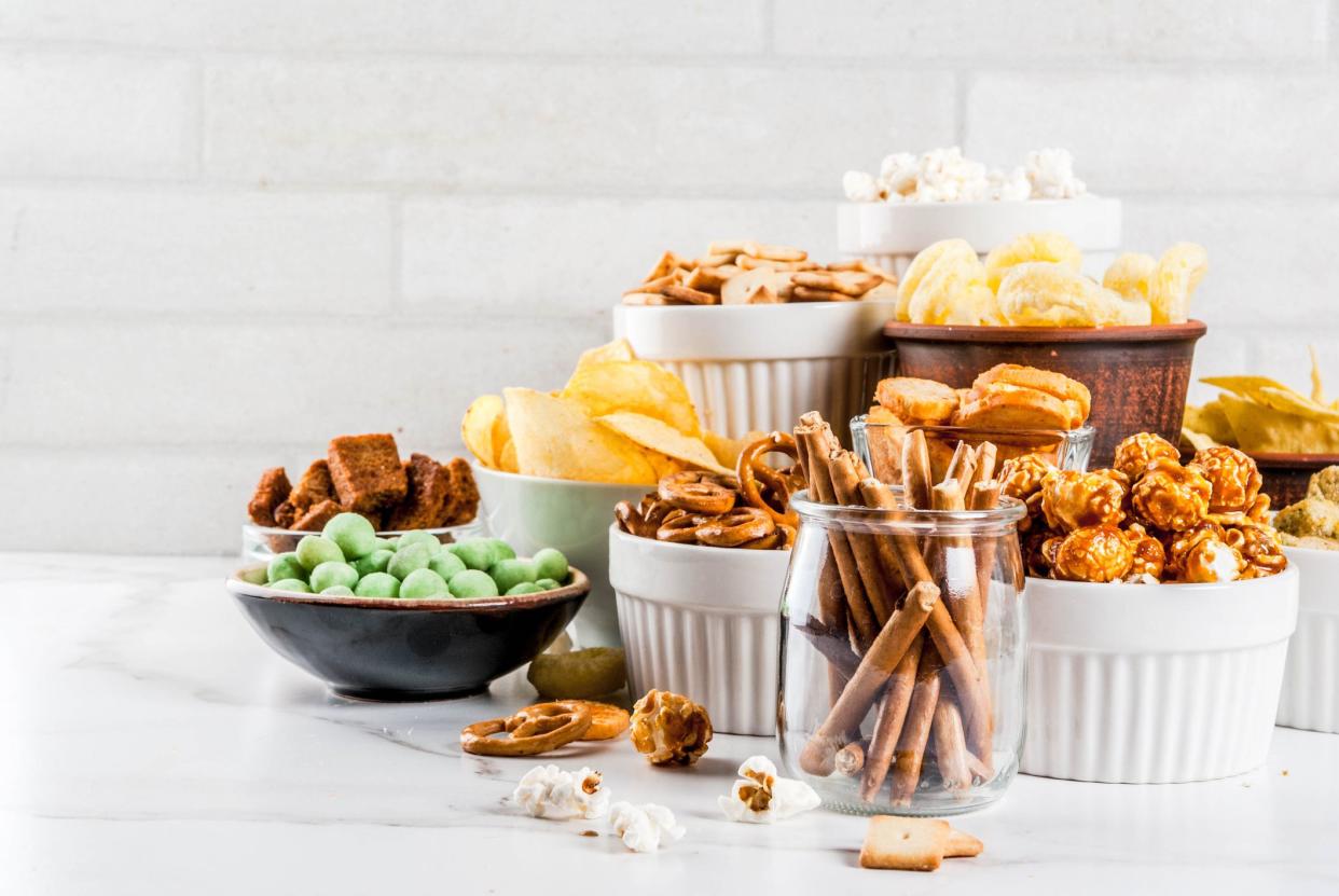 Variation different unhealthy snacks crackers, sweet salted popcorn, tortillas, nuts, straws, bretsels, white marble background copy space