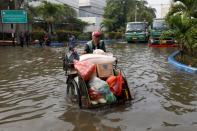 Man rides a rickshaw carrying vegetables and other goods through a road flooded at an area affected by land subsidence and rising sea levels in North Jakarta