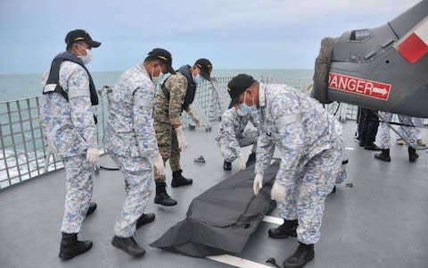  Navy sailors cover an unidentified body on to the deck of KD Lekiu frigate after it was recovered in the waters off the Johor coast of Malaysia - Credit: AP