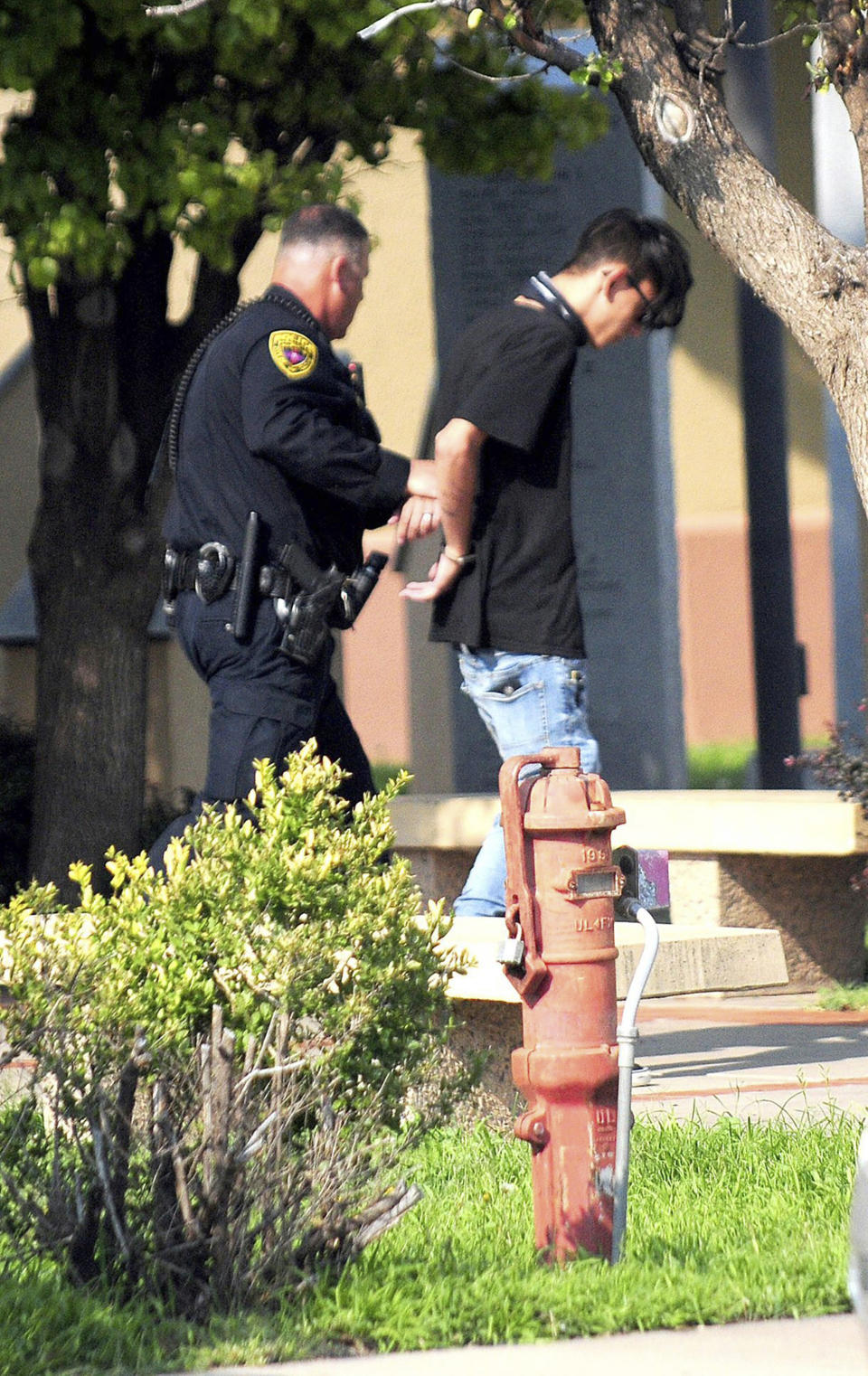 FILE - In this Monday, Aug. 28, 2017 file photo, police take a man, later identified as Nathaneil Ray Jouett, then 17, into custody after a shooting at a public library in the eastern New Mexico community of Clovis. Authorities say Jouett, then 17, who opened fire at a rural New Mexico library last year will plead guilty. The August, 2017 shooting killed two librarians and injured four others. District Attorney Andrea Reeb said Tuesday, Oct. 2, 2018 that Jouett has agreed to plead guilty to 30 counts listed in an indictment filed against him, including two counts of first-degree murder. (Tony Bullocks/Eastern New Mexico News via AP, File)