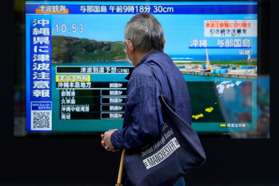 A person stands along a sidewalk to watch a TV showing a breaking news on tsunami for Okinawa, on April 3, 2024, in Tokyo. Japan issued tsunami alerts Wednesday after a strong quakes near Taiwan.<span class="copyright">Eugene Hoshiko—AP</span>