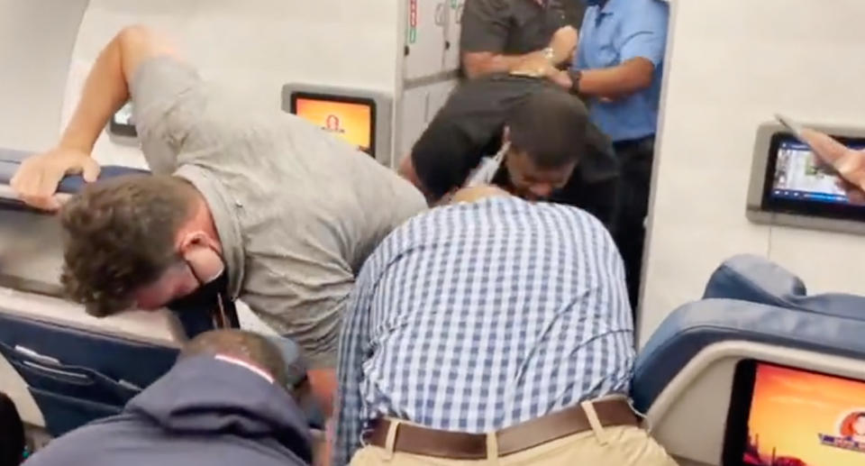 Passengers and flight attendants subduing an unruly man who forced a plane to be diverted after reportedly trying to open a door mid-air.