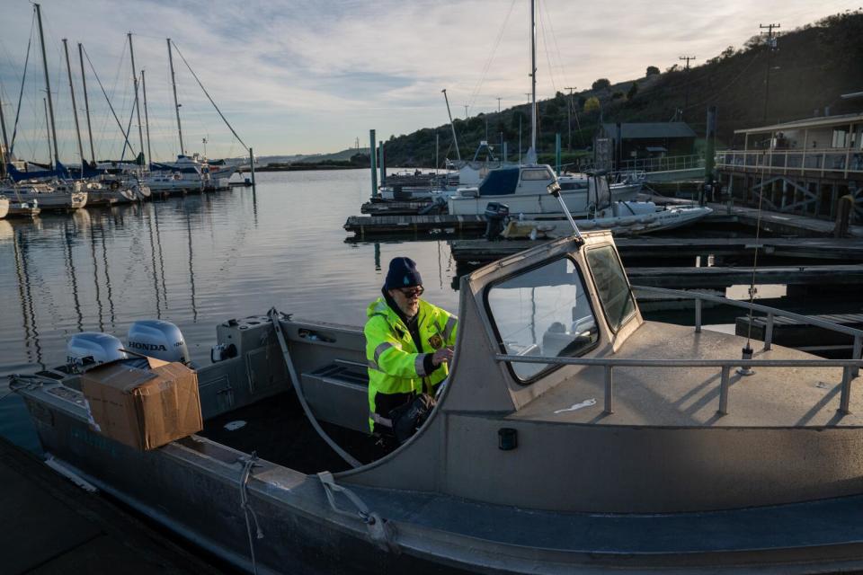 A person in a fluorescent yellow jacket at the wheel of a small boat