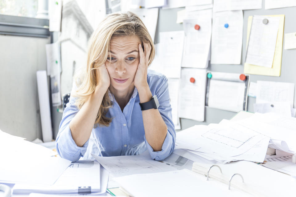 Stressed woman sitting at desk in office surrounded by paperwork