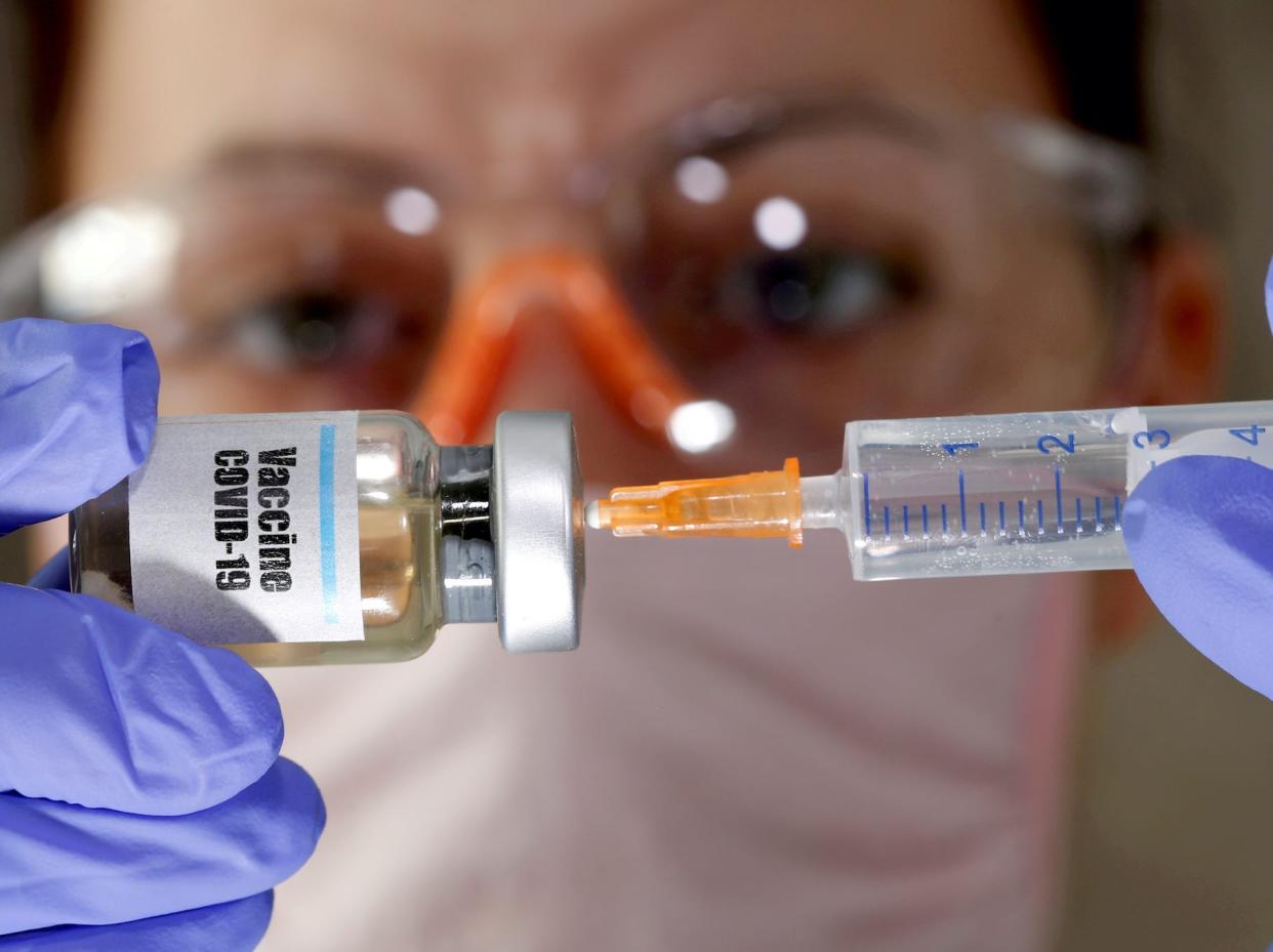 A woman holds a small bottle labeled with a "Vaccine COVID-19" sticker and a medical syringe in this illustration taken April 10, 2020.