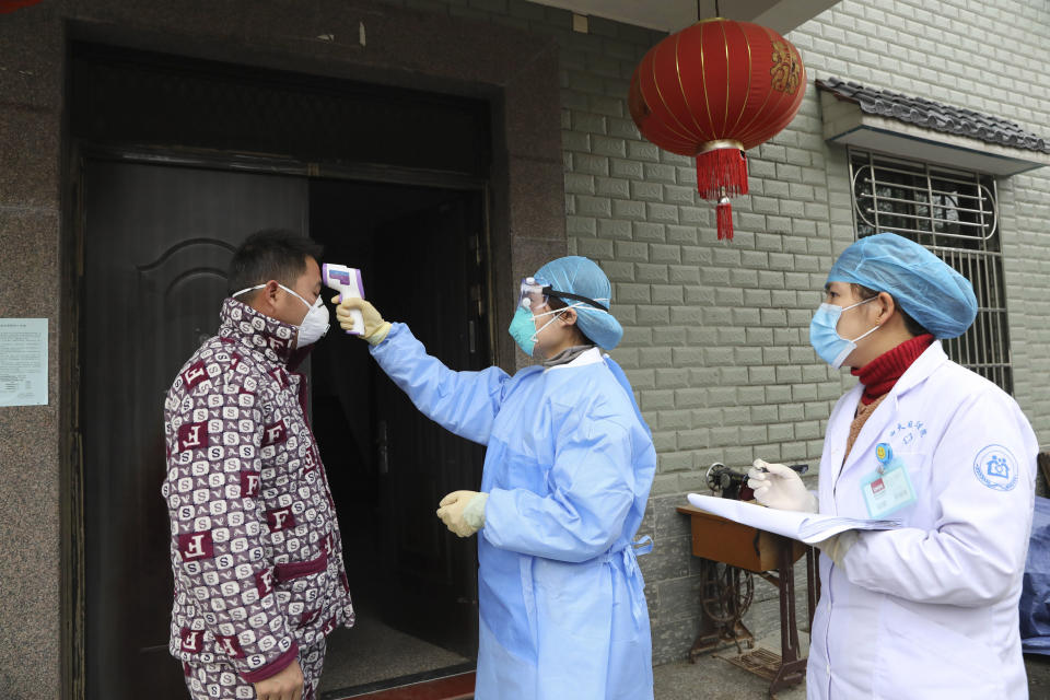 Community health workers check the temperature of a person who recently returned from Hubei Province, center of a virus outbreak, in Hangzhou in eastern China's Zhejiang Province, Monday, Jan. 27, 2020. China on Monday expanded sweeping efforts to contain a viral disease by extending the Lunar New Year holiday to keep the public at home and avoid spreading infection. (Chinatopix via AP)