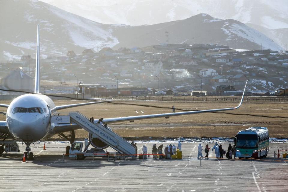 Officials in hazmat suits greet passengers on a plane against the backdrop of Mongolian capital Ulaanbaatar,.