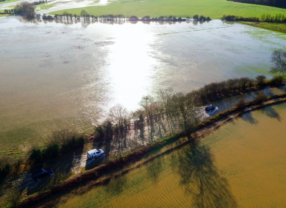 Vehicles negotiate the flooded B4069 road at Christian Malford in Wiltshire after the river Avon burst its banks (PA)