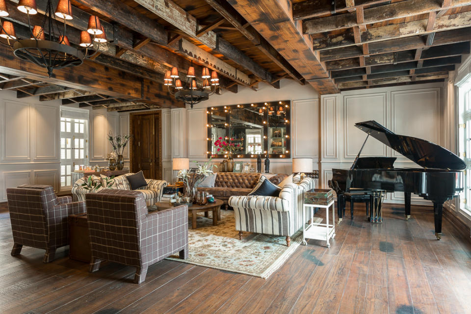 Floor-to-ceiling wooden cladding gives the capacious living room its classic, mountain vibe. The furniture, lighting and accent pieces were designed to highlight the focal point of this space: a custom-made, reclaimed timber ceiling. Chandeliers and chequered sofas by <a href="https://fave.co/2PhLLYB" rel="noopener" target="_blank" data-ylk="slk:Peacock Life;elm:context_link;itc:0;sec:content-canvas" class="link ">Peacock Life</a>; carpet by <a href="https://fave.co/2K23nnU" rel="noopener" target="_blank" data-ylk="slk:Jaipur Rugs;elm:context_link;itc:0;sec:content-canvas" class="link ">Jaipur Rugs</a>.