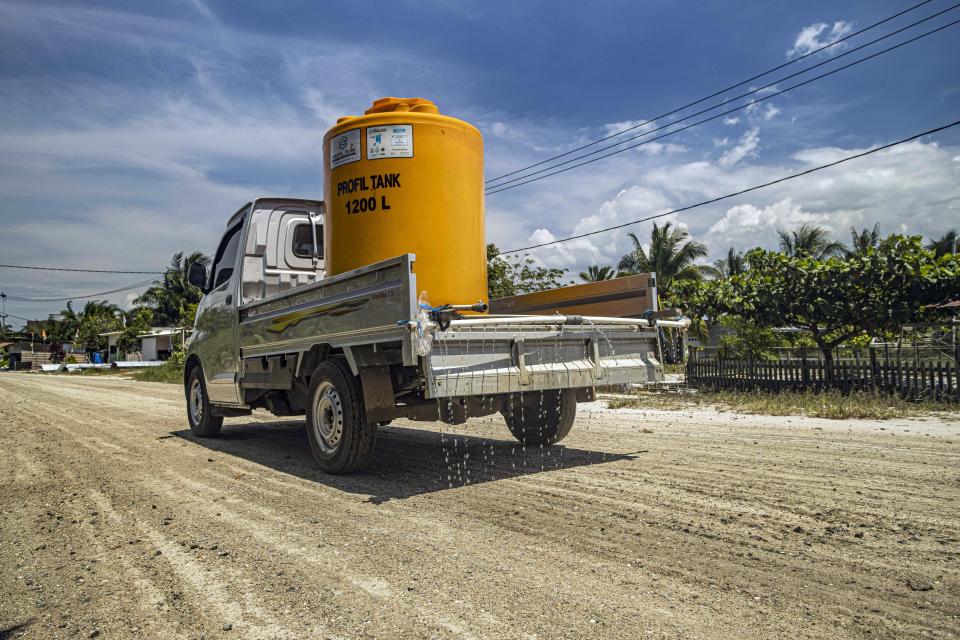 A truck carrying a water tank sprays the dirt road to reduce dust at Mangkupadi village near the construction site of the Kalimantan Industrial Park Indonesia (KIPI) in North Kalimantan, Indonesia on Thursday, Aug. 24, 2023. Residents hope the project may bring jobs, but worry they will lose their traditional livelihoods as fishermen, farmers and increasingly, eco-tourism hosts as dust and ash smother their fields. (AP Photo/Yusuf Wahil)