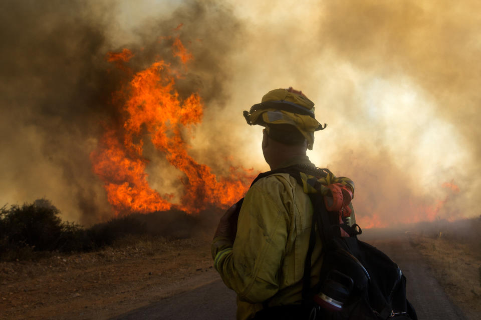 A firefighter watches the Apple Fire in Cherry Valley, Calif., Saturday, Aug. 1, 2020. A wildfire northwest of Palm Springs flared up Saturday afternoon, prompting authorities to issue new evacuation orders as firefighters fought the blaze in triple-degree heat. (AP Photo/Ringo H.W. Chiu)