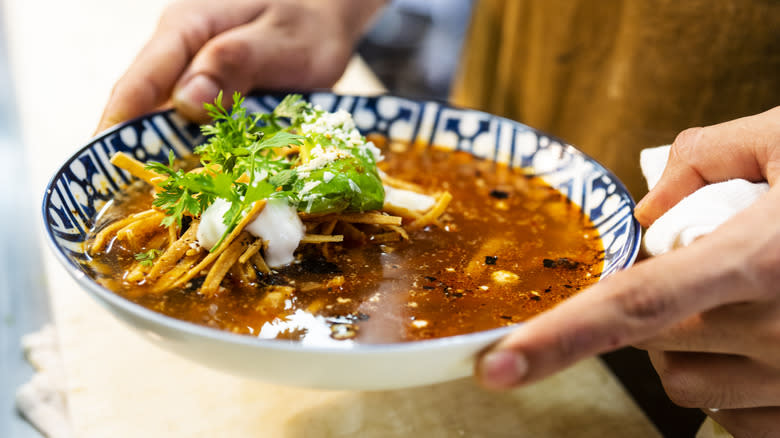 Hands holding a bowl of tortilla soup