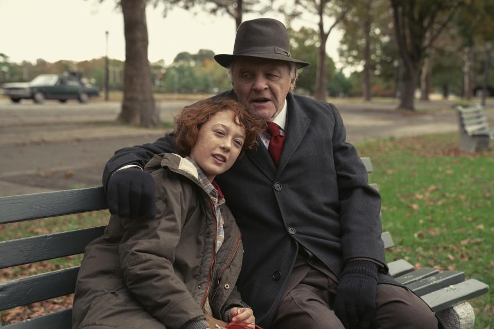 An elderly man and his grandson sit close on a park bench, sharing a moment of comfort