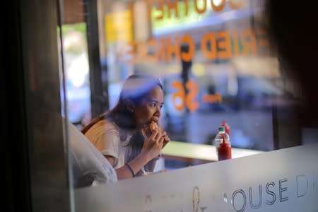 FILE PHOTO: A woman can be seen through the window of a fast-food restaurant eating a burger in Sydney, Australia