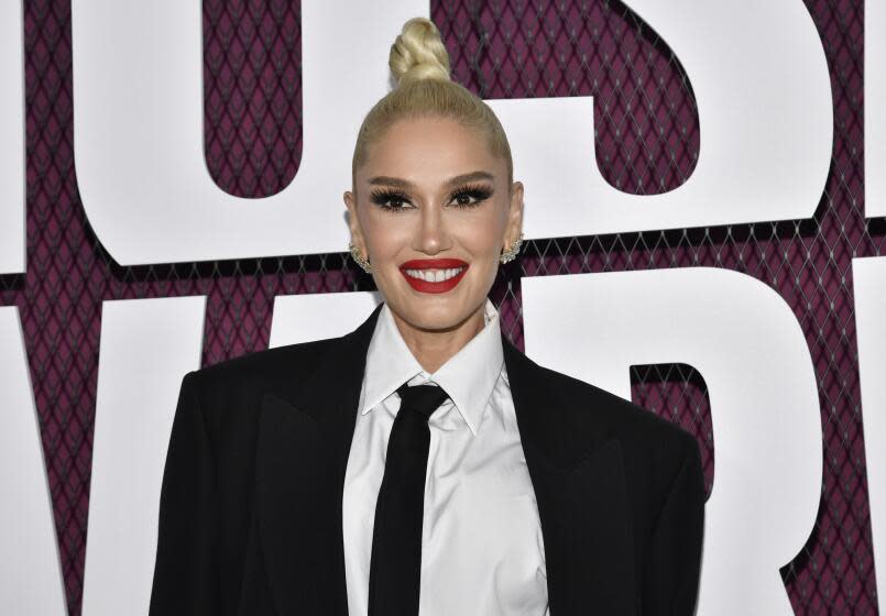 Gwen Stefani with her hair in a high bun and slicked back. She's wearing a black suit jacket, white shirt and black tie.