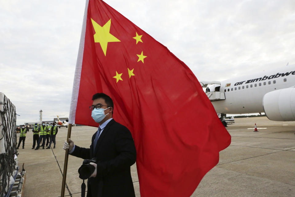 An official from the Chinese Embassy in Zimbabwe holds a Chinese flag next to a plane carrying Sinopharm COVID-19 vaccine from China upon arrival at Robert Mugabe International airport in Harare, Monday, Feb, 15, 2021. Zimbabwe has received its first COVID-19 vaccines with the arrival early Monday of an Air Zimbabwe jet carrying 200,000 Sinopharm doses from China. (AP Photo/Tsvangirayi Mukwazhi)