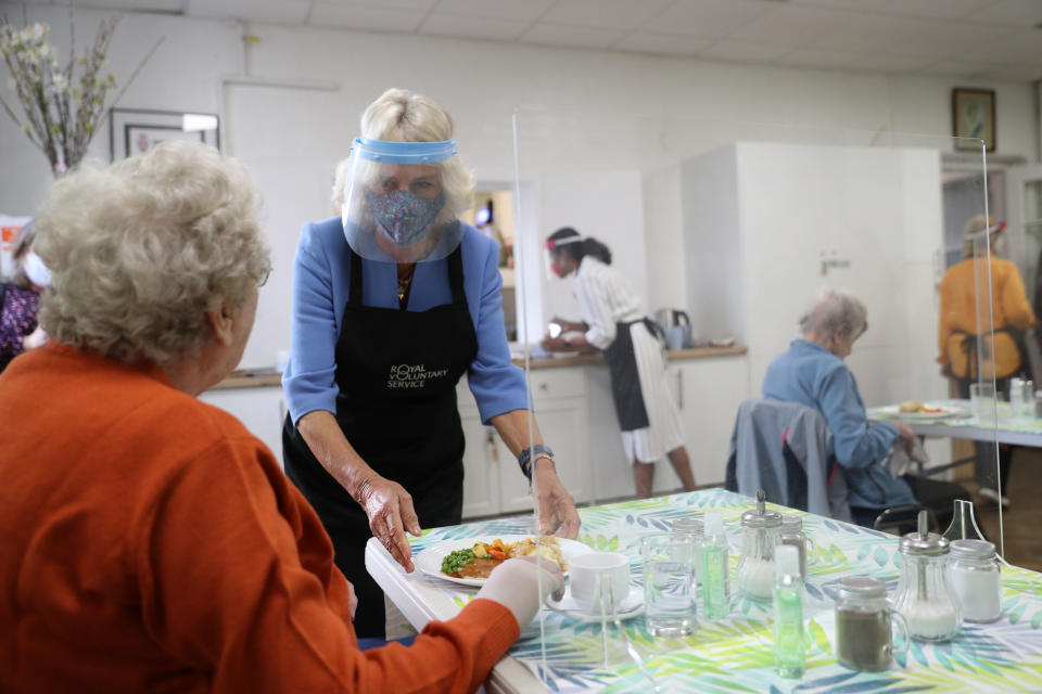 Britain's Camilla, Duchess of Cornwall, in her role as President, Royal Voluntary Service, wears a facemask and faceshield as she serves lunch to Doris Winfield, 86, during her visit to the Royal Voluntary Service Mill End lunch club in Rickmansworth, Hertfordshire on October 8, 2020, to meet volunteers who have overcome recent challenges posed by the novel coronavirus COVID-19 pandemic to reinstate the much-needed lunch sessions. (Photo by Andrew Matthews / POOL / AFP) (Photo by ANDREW MATTHEWS/POOL/AFP via Getty Images)