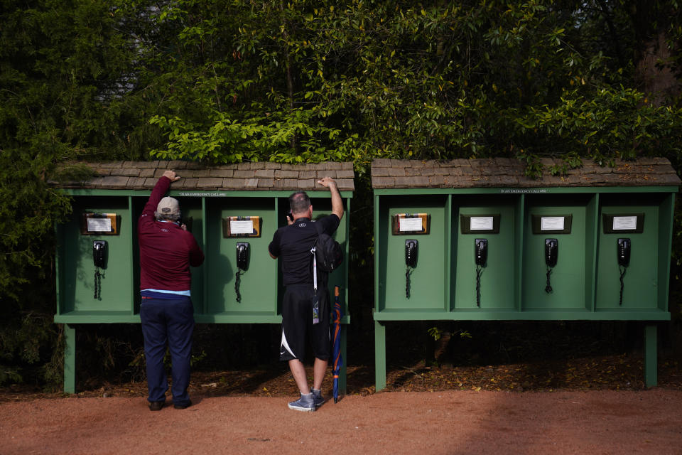 With mobile phone prohibited on the Augusta National Golf Course, spectators use phones provided by the club near the seventh hole during a practice round for the Masters golf tournament on Tuesday, April 5, 2022, in Augusta, Ga. (AP Photo/Jae C. Hong)